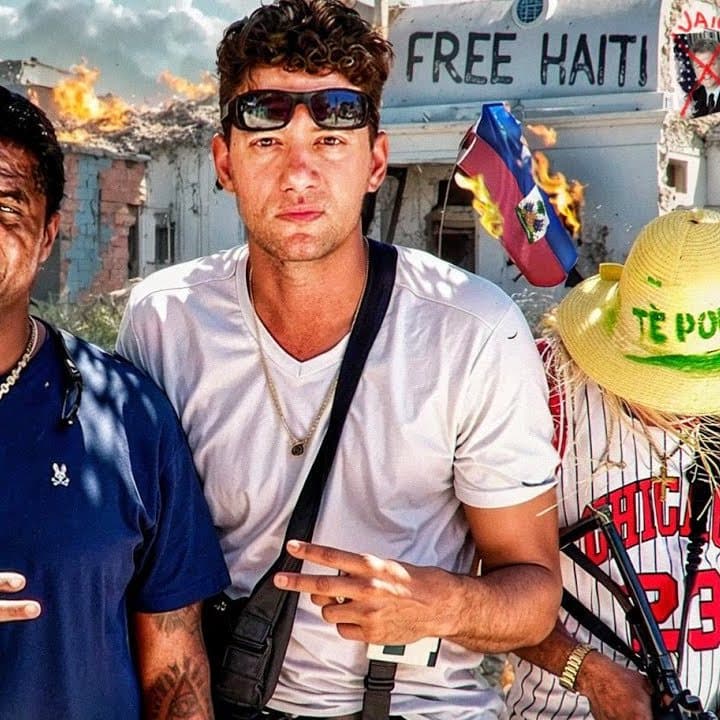 Timmy Karter in a white T-shirt with sunglasses on his head, in front of a 'Free Haiti' wall, from the thumbnail of his Haiti video