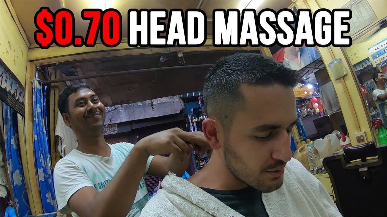 Volpe with a fresh short haircut and a white towel round his shoulders, eyes shut, while a smiling barber in a white T-shirt massages the back of his neck in a small yellow-walled shop in Siliguri, under the words $0.70 head massage