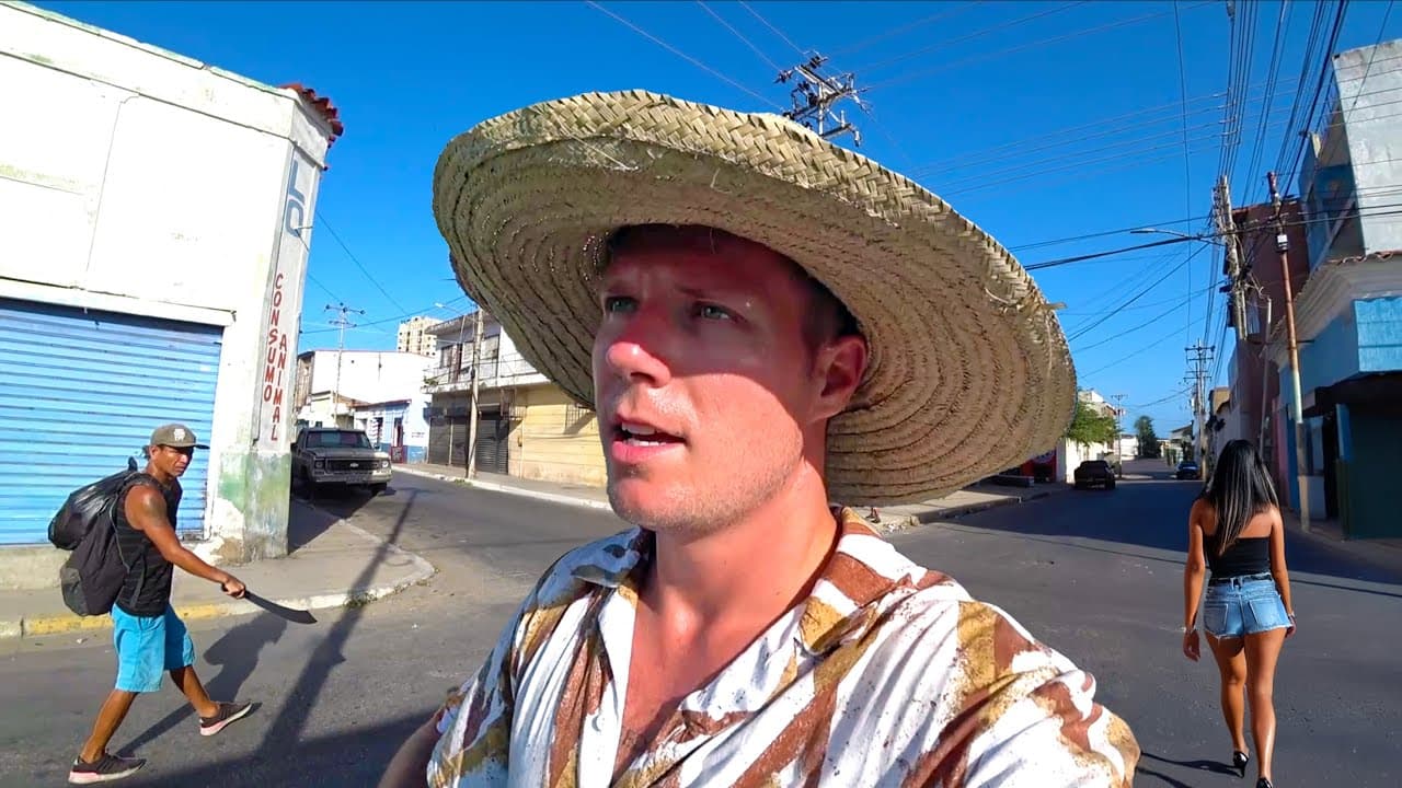 YouTube thumbnail for 'Gringo Goes to Venezuelan Mafia Island!' showing Kurt Caz in a wide straw hat on a street in Venezuela, with a man carrying a machete and a woman walking past in the background